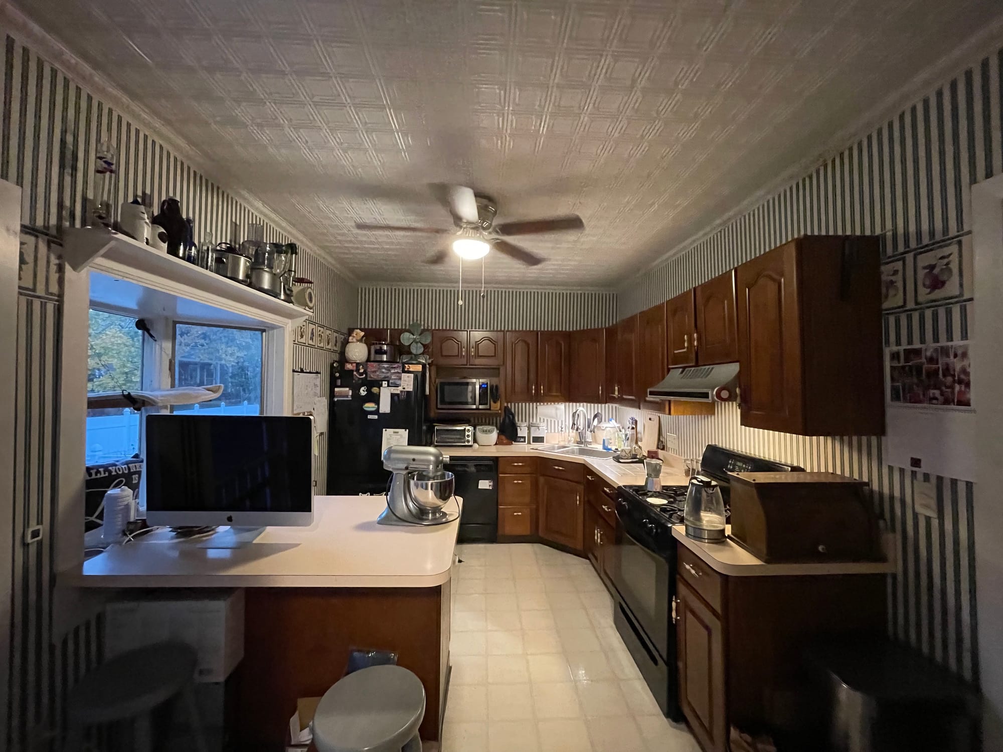 A wide shot of a kitchen with green striped wallpaper and brown cherry cabinets.