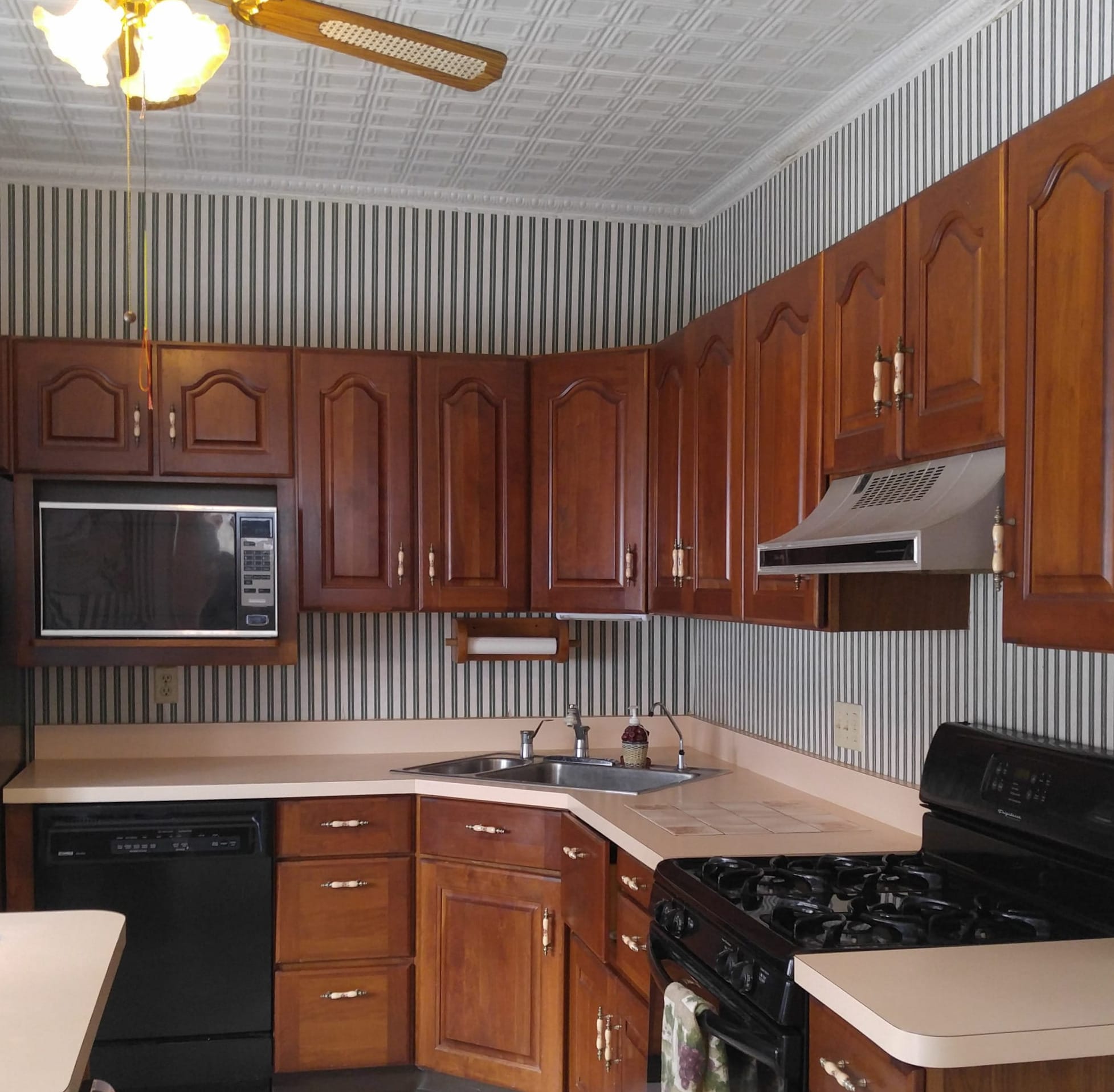 Cherry brown cabinets, pink countertop, and striped green wallpaper adorned this kitchen. 