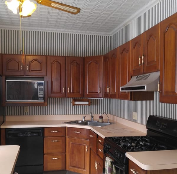 Cherry brown cabinets, pink countertop, and striped green wallpaper adorned this kitchen. 