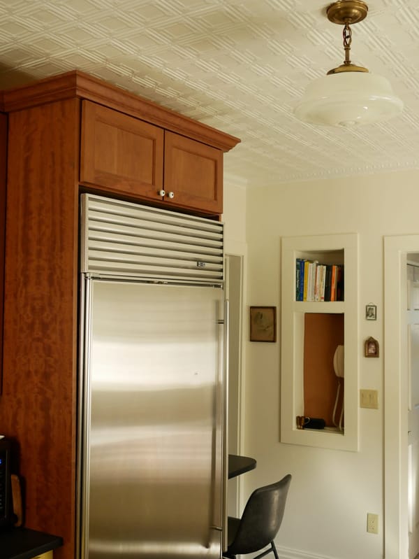 A stainless steel Subzero refrigerator in a cherry wood build-out cabinet, a phone nook on an ivory painted wall in the background